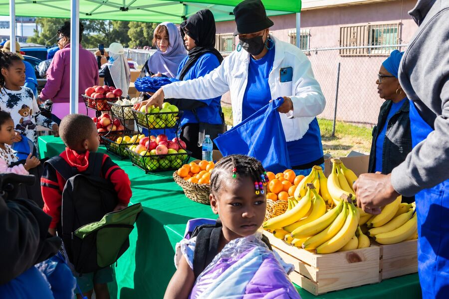 A volunteer in a white coat handing out fresh fruit and produce to a young girl at a Food & Nutrition table.